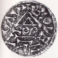 Černobílá fotografie. Mince pokrytá různými znaky a nečitelnými písmeny.