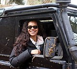 Woman sat in her car wearing sunglasses smiling towards the camera.