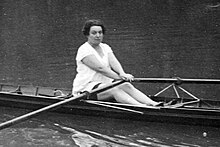 Photo en noir et blanc d'une femme blanche aux cheveux bruns vêtue de blanc, pratiquant l'aviron.