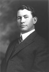 A man with dark, wavy hair wearing a dark jacket and tie and white shirt