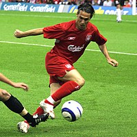 A man in a red shirt and shorts on a field looking down at a ball