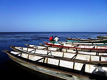 Des barques longilignes attendent sur la barge, deux hommes discutent en regardant le lac.