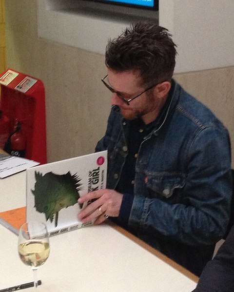 File:Jamie Hewlett in 2014 signing copies of "The Cream of Tank Girl" at a Tank Girl lecture at the British Library- 2014-07-03 08-13.jpg