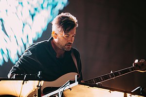 Bonobo appearing to perform onstage, holding a bass guitar