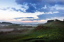 Photographie d'une vallée entourée de collines à gauche et à droite au crépuscule avec de la brume.