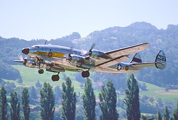 A shiny aircraft taking off, with mountains behind it