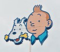 Représentation de Tintin (jeune homme imberbe roux coiffé à la houppette) et son chien Milou (fox-terrier à poil dur avec un os dans sa bouche) sur l'enseigne d'un immeuble.