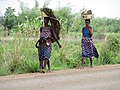 Deux femmes marchant pieds nus, la première avec bébé au dos, de retour du champ sous un soleil ardent à Pobè au Bénin.