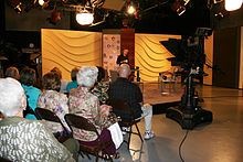 An audience seated in front of a set in a television studio