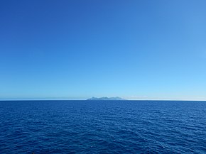 Étendue d'un océan, et une île en son centre au loin.