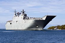 A grey warship sailing near the shoreline.