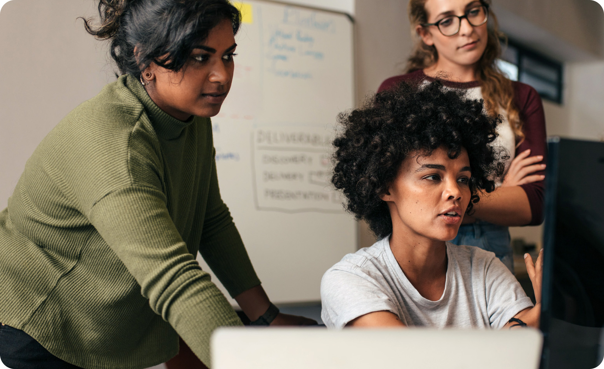 Two people looking over the shoulder of another person, all looking at a computer monitor