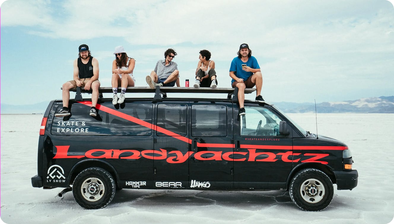 A Landyachtz-branded van in the salt flats with five people sitting on top of it talking