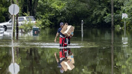 Savannah Fire Advanced Firefighters Andrew Stevenson, front, and Ron Strauss carry food to residents in the Tremont Park neighborhood that where stranded in flooding from Tropical Storm Debby, Tuesday, Aug. 6, 2024, in Savannah, Ga. (AP Photo/Stephen B. Morton)