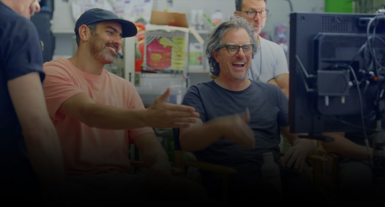 Imagen de dos cineastas sentados que miran y gesticulan hacia una pantalla de proyección.