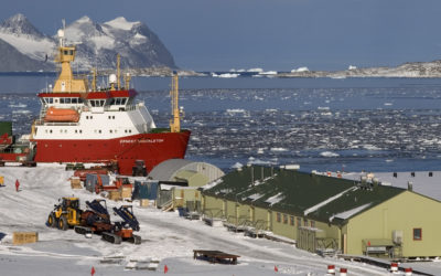 A landscape of an Antarctic base with a large ship docked nearby