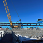 A yellow construction crane in front of a new blue building with blue sky above