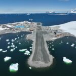 view of a runway from the air with icy waters and snowy mountain surrounding the runway.