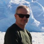 A man wearing sunglasses and standing in front of a mountain