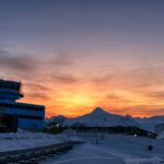 A sunset over the snow with a blue building on the left