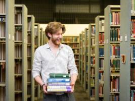 Student walking through library book stacks carrying books