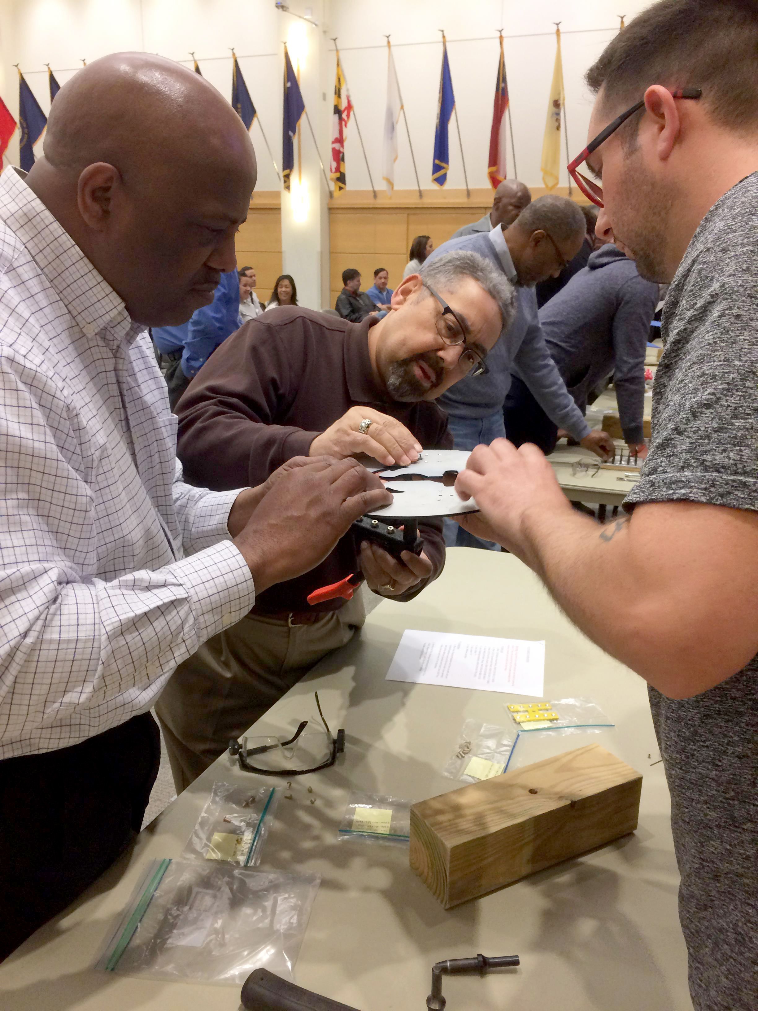 Three employees gathered around a table construct military service insignia with hardware