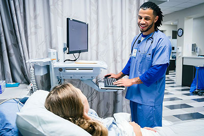 A nurse stands by a hospital bed talking to a patient