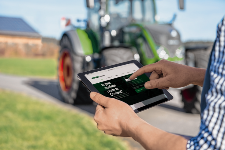 Delante de un tractor Fendt, se ve a un hombre que sostiene una Tablet que muestra cómo se verifica Fendt Connect en sus máquinas.