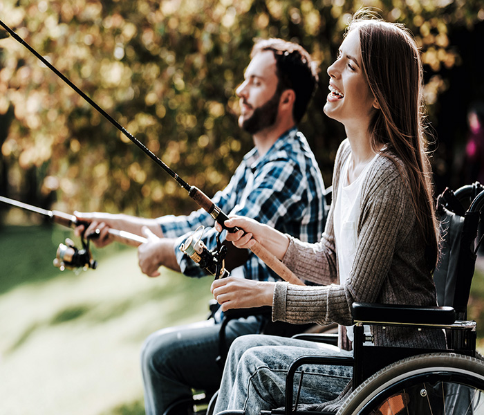 Two people on wheelchairs, each holding a fishing rod and fishing.