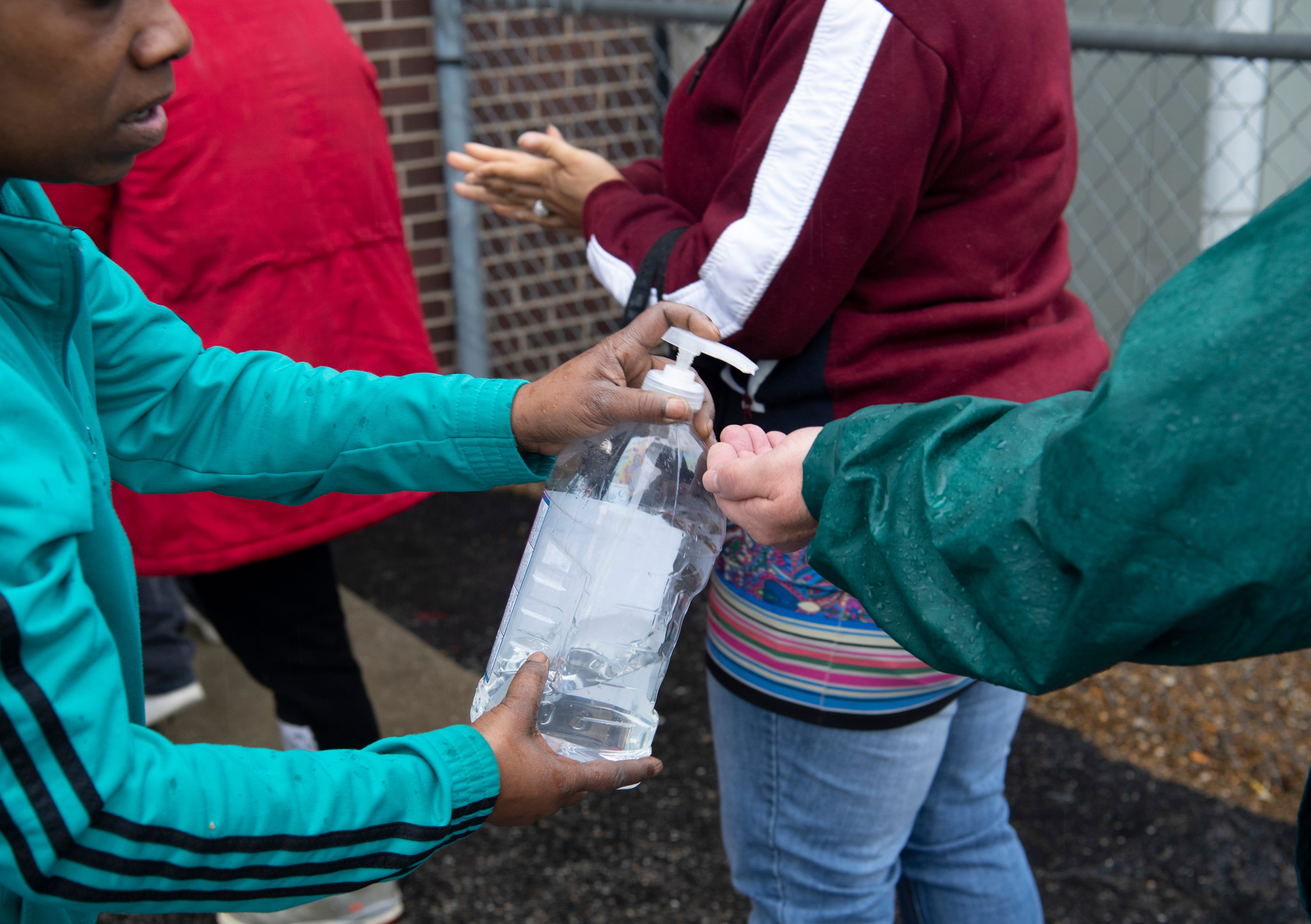 Lashawn Miles offers squirts of hand sanitizer to people participating in the lunch program at the Salvation Army in Evansville, Ind. on March 18, 2020.