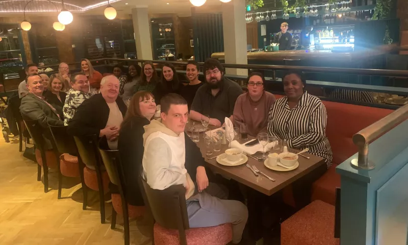 The Lived Experience Panel members sitting around a table at a restaurant, all looking and smiling for the camera.