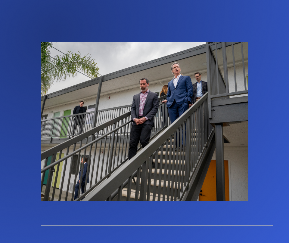 Governor Newsom walks down stairs outside of an apartment complex with a man.