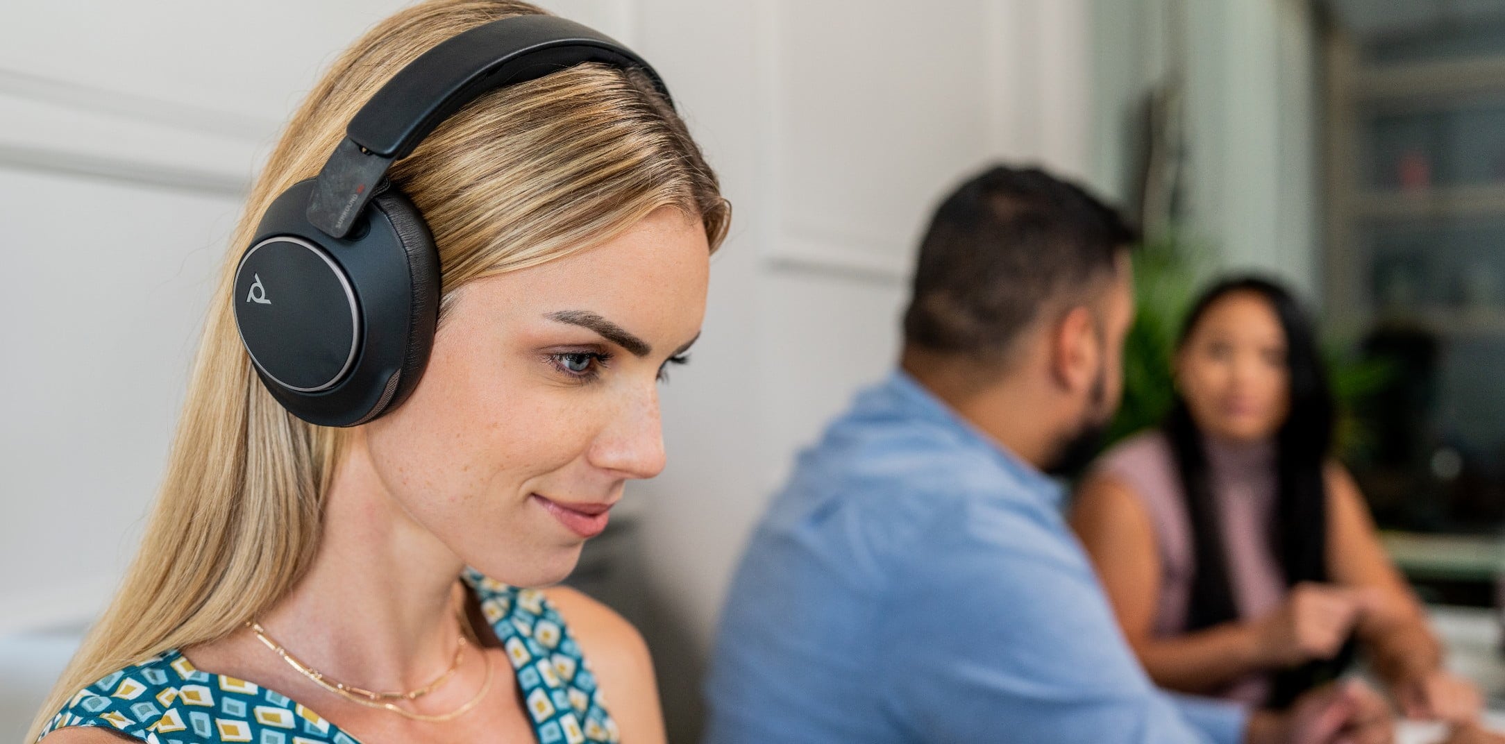 Woman in office wearing Poly Voyager Surround 80 noise cancelling headset