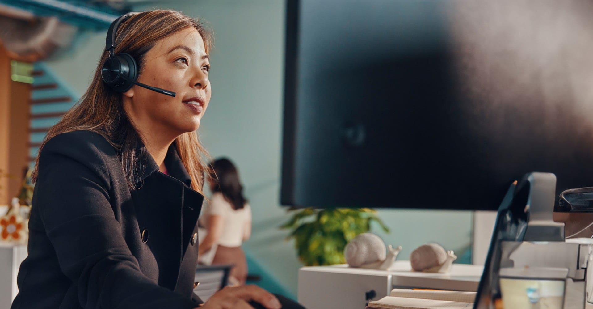 Woman in open office at desk wearing Poly Savi 7300 UC wireless headset