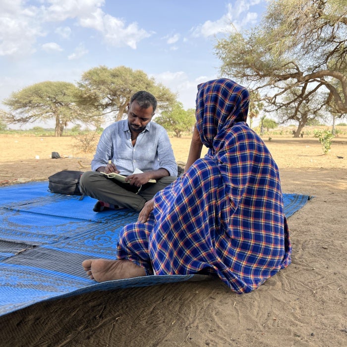 A researcher takes notes while sitting with an interviewee