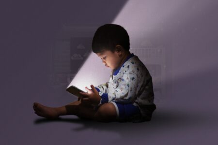 Child interacting with a tablet device with tablet's light shining on the child