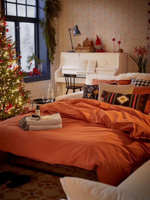 Weisse 2-Sitzer-Schlafcouch HYLTARP, die zu Weihnachten im Wohnzimmer zu einem Bett mit rotbraunem Bettbezug ÄNGSLILJA ausgezogen wurde.