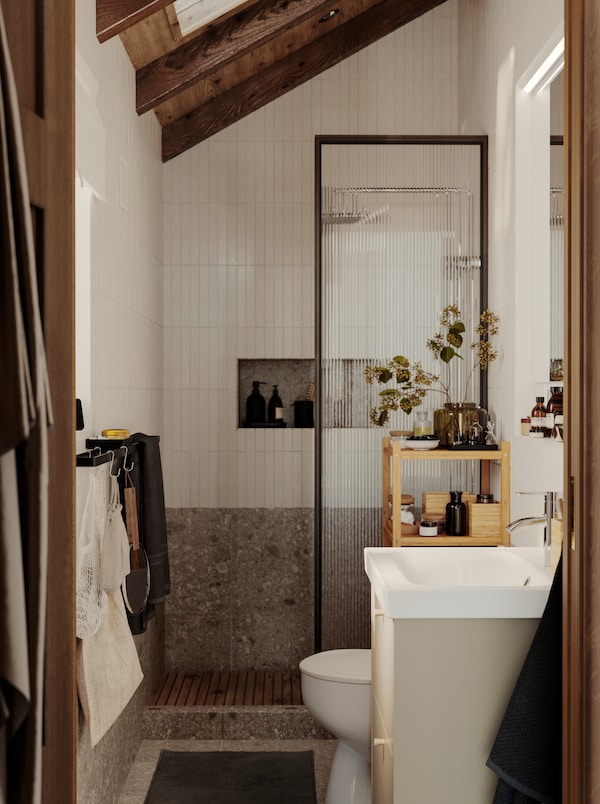 A small bathroom with white tiles, a grey stone floor and a wooden ceiling has a shower, a HAVBÄCK wash-stand and a mirror.