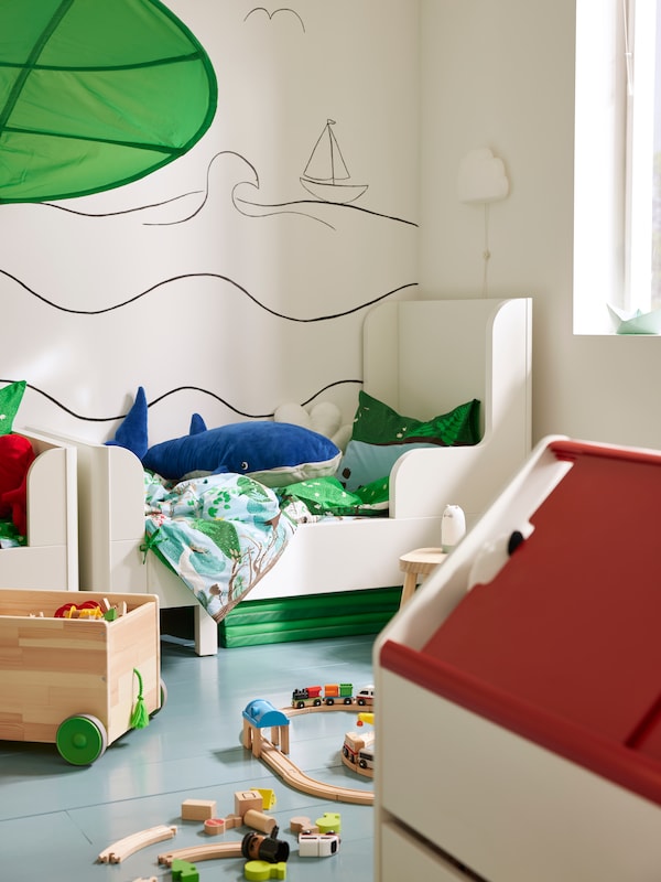 View of children’s room in daylight with toys everywhere, beds in the back and LILLABO storage unit in foreground.