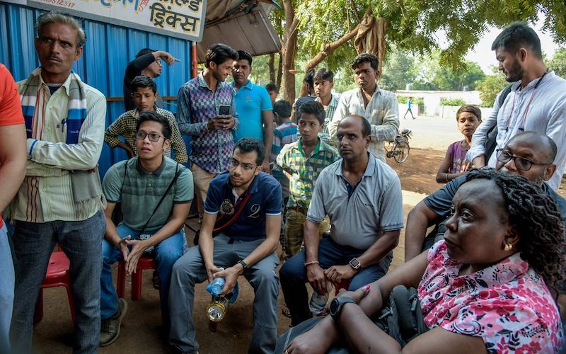 a group of men and a woman from India sitting or standing while listening to someone