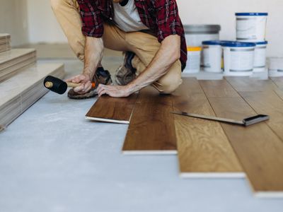 A man installs floor panels using a mallot