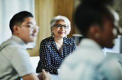 Smiling mature female business owner listening during presentation during meeting in office conference room