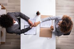 Aerial view of two business people shaking hands at a desk with papers on it