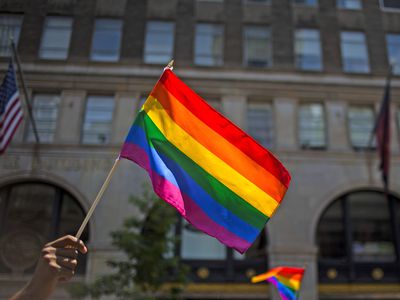 Hand holding rainbow flag outdoors in front of building