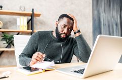 Young Black man in a sweater looking at a laptop screen in a stressed-out manner