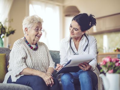 White-haired woman and nurse sit on a couch, going over paperwork