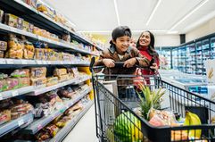 A young boy playing on a shopping cart in a grocery store