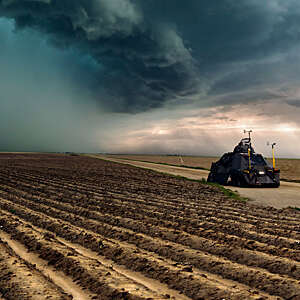 Tornado-chasing vehicle with IMAX camera drives along ploughed fields towards a looming storm in Colorado, USA