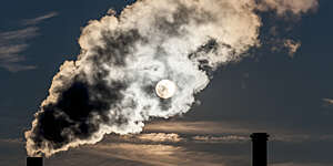 Dense smoke is leaving a smoke stack of a power plant.