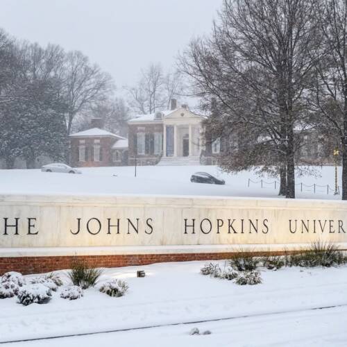 Snow falls on a marble sign reading The Johns Hopkins University